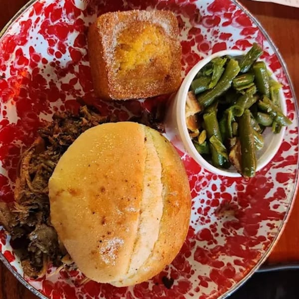 Cindy Lou's BBQ plate with pulled pork, a bun, cornbread, and green beans on a red splatter plate.
