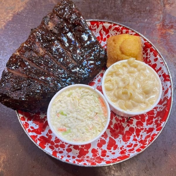Cindy Lou's BBQ ribs, mac and cheese, coleslaw, and cornbread on a red and white speckled plate.