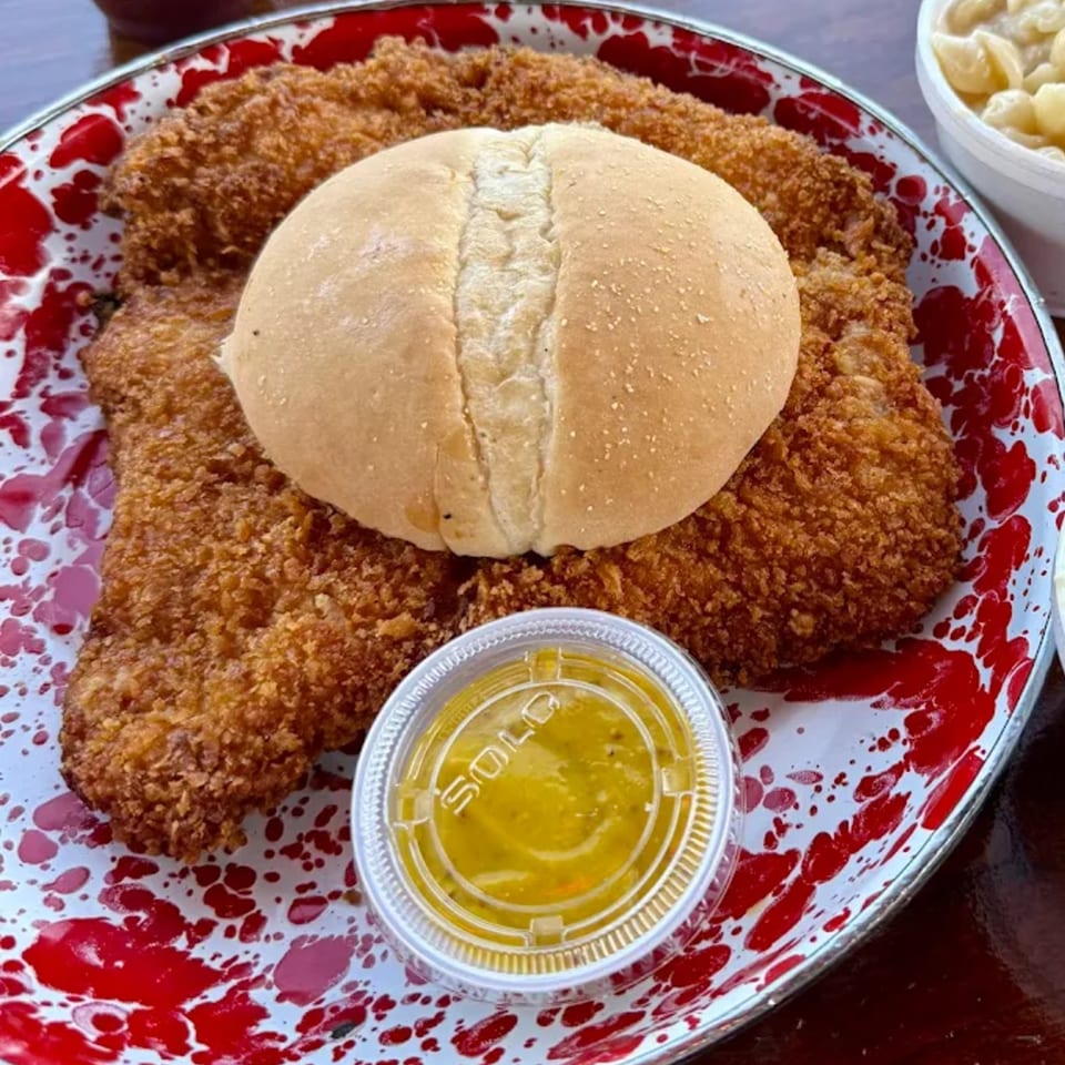 Cindy Lou's BBQ fried pork tenderloin sandwich on a red and white splatter plate with sauce.