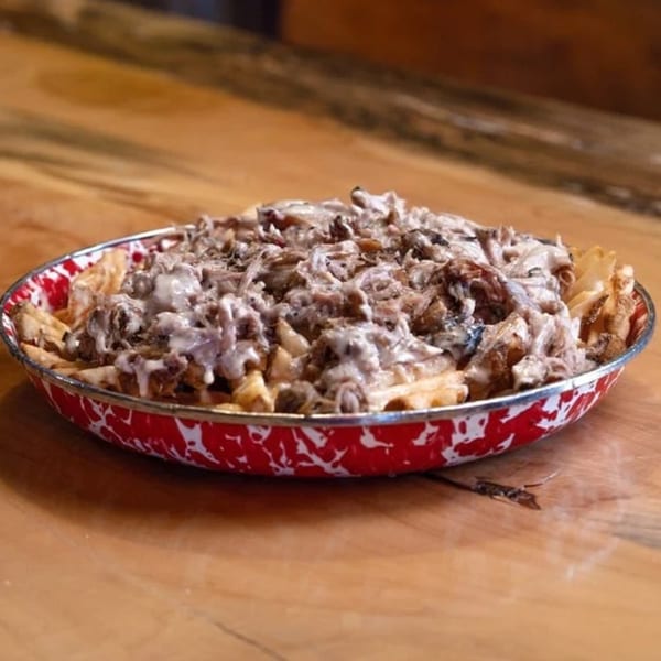 Cindy Lou's BBQ pulled pork fries, topped with creamy sauce, served in a red and white speckled bowl.