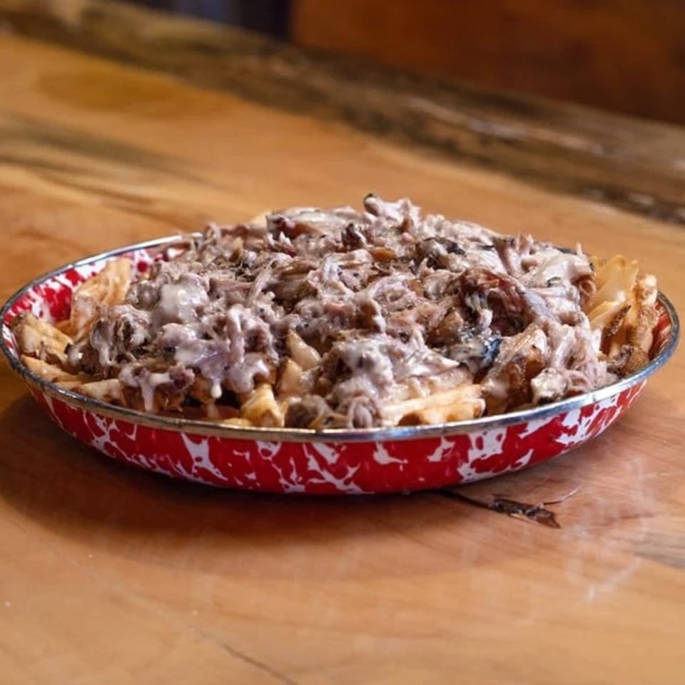 Cindy Lou's BBQ pulled pork fries, topped with creamy sauce, served in a red and white speckled bowl.