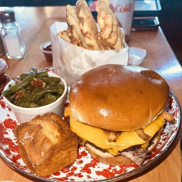 A Cindy Lou's BBQ cheeseburger with fries, green beans, and cornbread on a splatter-painted plate.