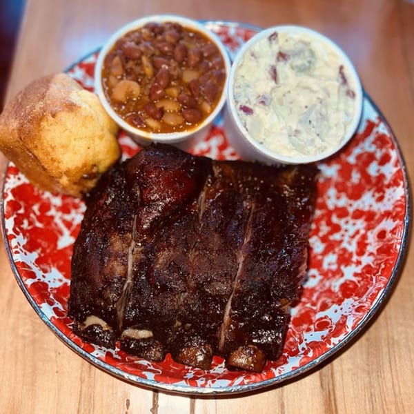 Cindy Lou's BBQ ribs, baked beans, potato salad, and cornbread on a red and white plate.