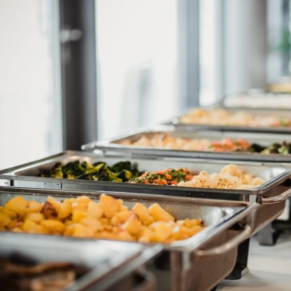 A buffet line of chafing dishes filled with roasted potatoes, mixed vegetables, and broccoli.