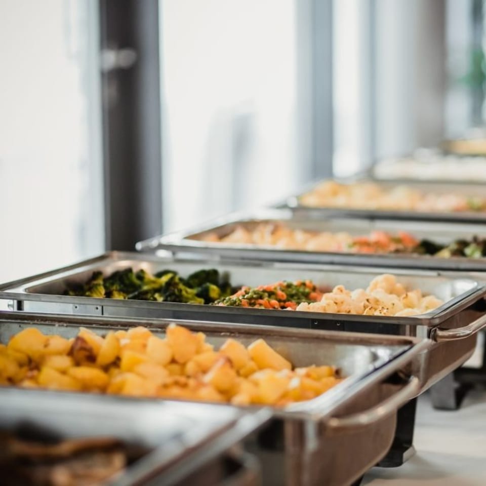 A buffet line of chafing dishes filled with roasted potatoes, mixed vegetables, and broccoli.